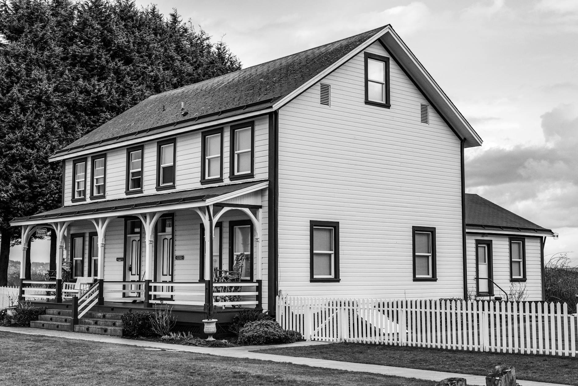 Black and white photo of a classic wooden house with picket fence.