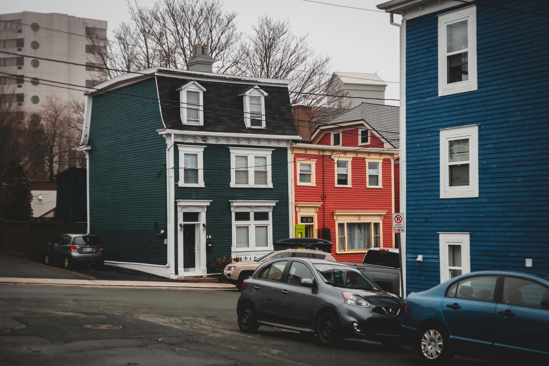 Colorful old fashioned residential houses located on street near asphalt road with parked automobiles in town with tall leafless trees