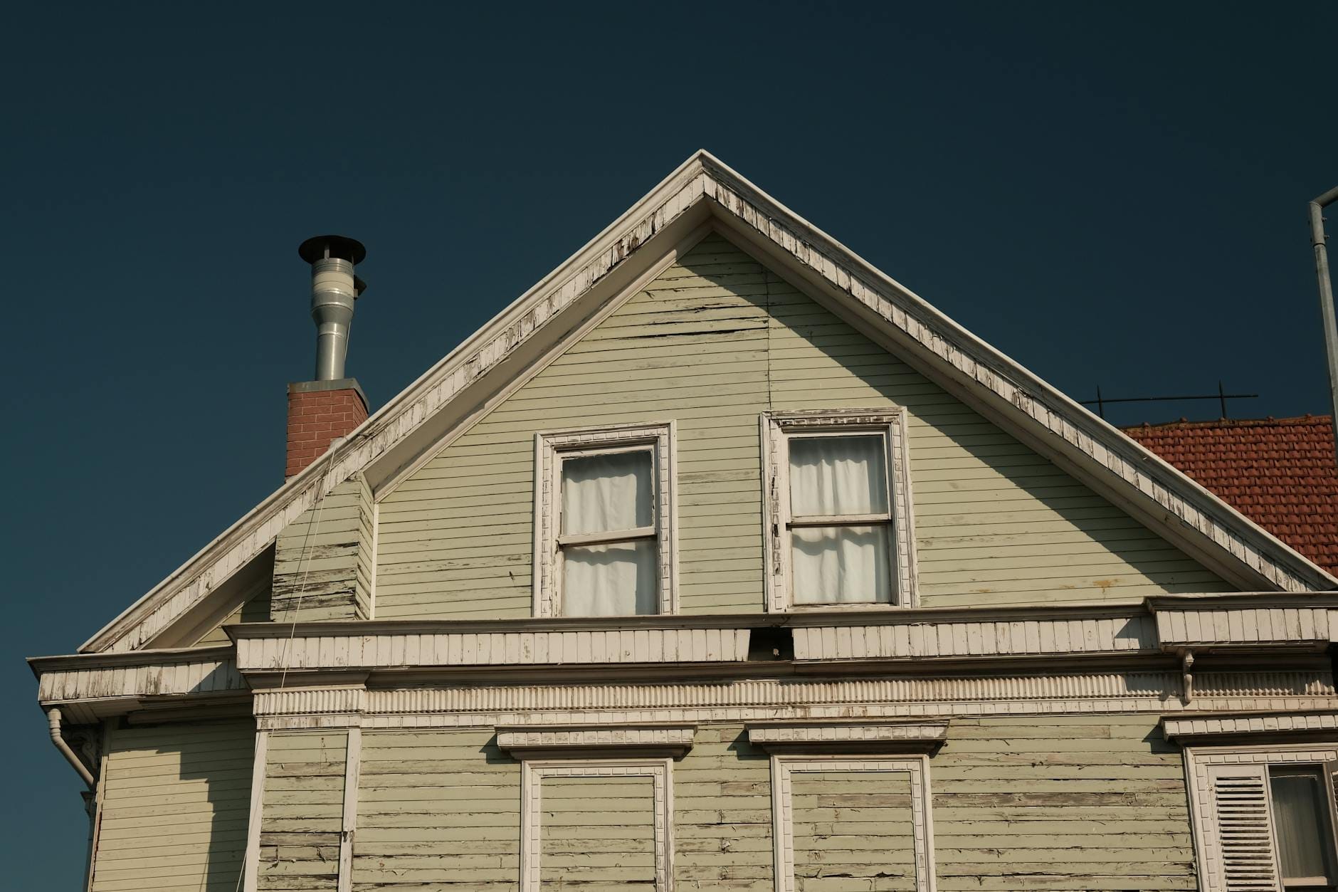 Sunlit vintage house with gable roof and chimney, showcasing retro charm.