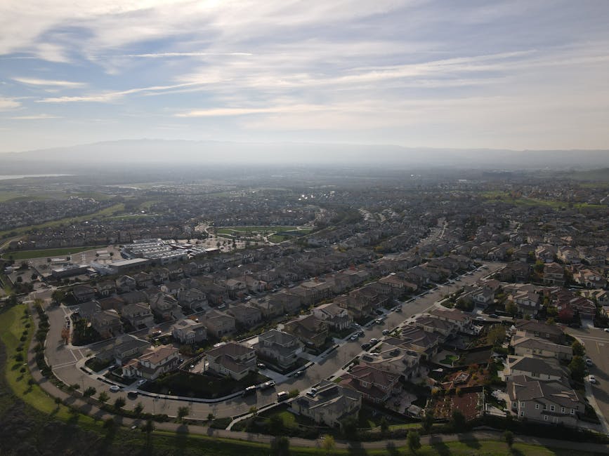 Suburban houses on a green lawn with hills behind.