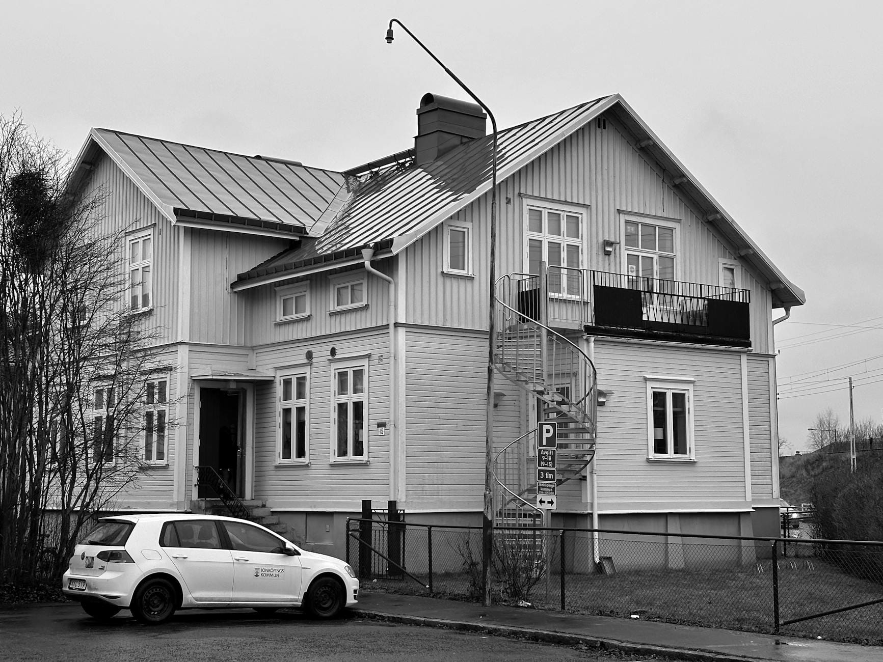Monochrome image of a suburban house with a spiral staircase and parked white car, capturing architectural details.