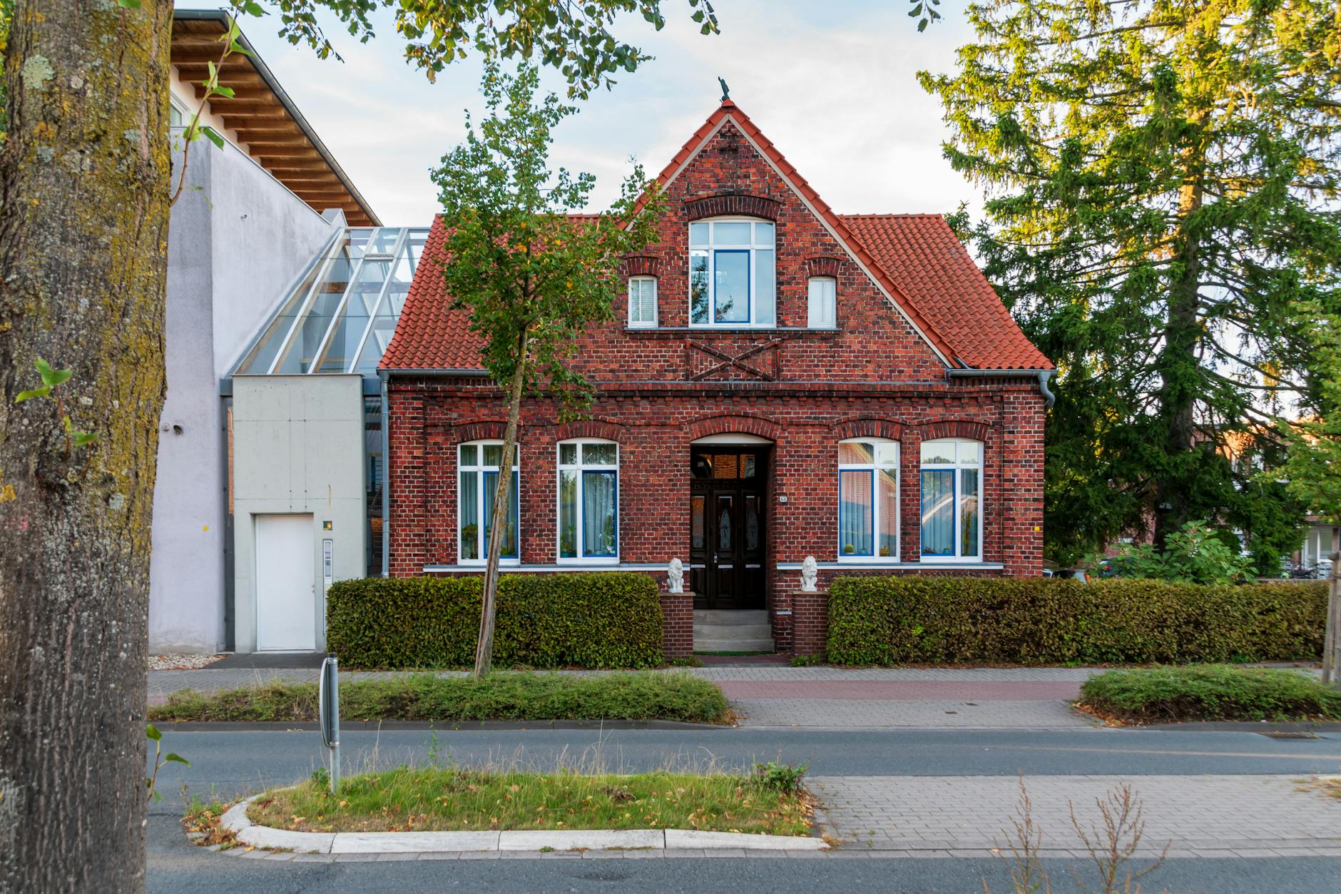 Red brick house with triangular roof and white-trimmed windows, surrounded by greenery.