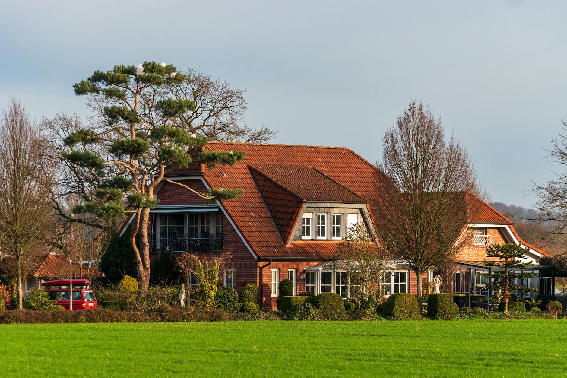A picturesque country house with a red roof amidst lush green landscape and trees, captured on a sunny day.